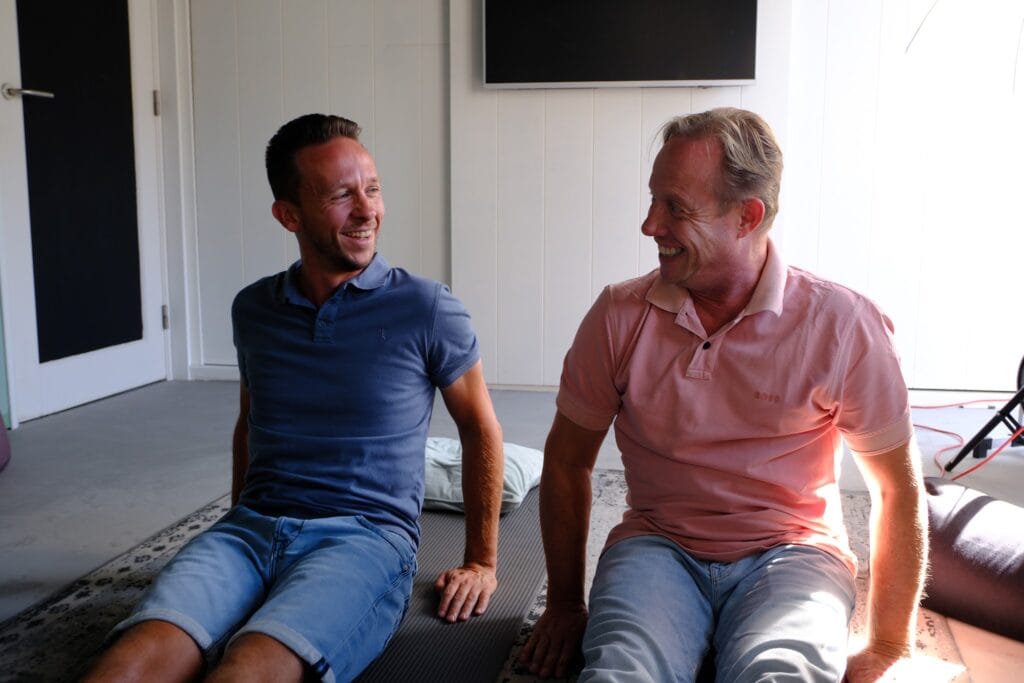 Arjen en een cliënt lachen samen na een ademoefening op de mat